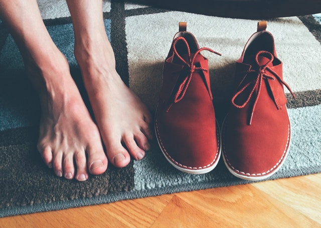 Bosé nohy, vedľa ktorých sú položené červené topánky