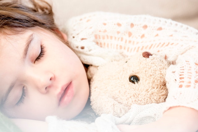 Malé dievča v pletenom svetri spí s plyšovým medveďom.jpg